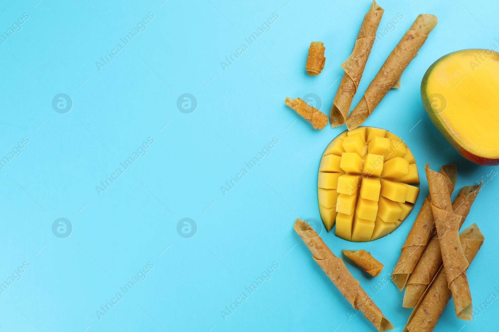 Photo of Delicious fruit leather rolls and mango on light blue background, flat lay. Space for text