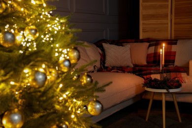 Photo of Sofa, candles on table and glowing Christmas tree in living room