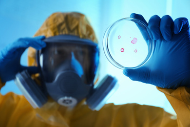 Photo of Scientist in chemical protective suit with Petri dish at laboratory, focus on hand. Virus research