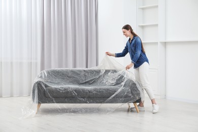 Young woman putting plastic film away from sofa at home
