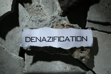 Photo of Paper with word Denazification on pieces of concrete, top view
