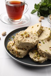 Photo of Tasty halva with pistachios served on white tiled table, closeup