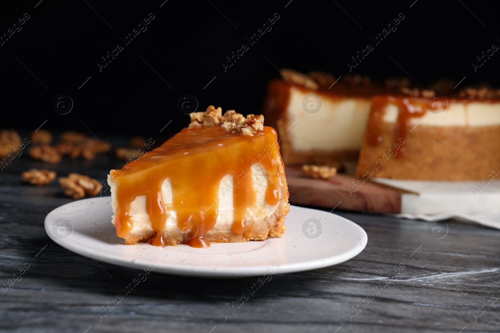 Photo of Piece of delicious cake with caramel and walnuts on black marble table, space for text