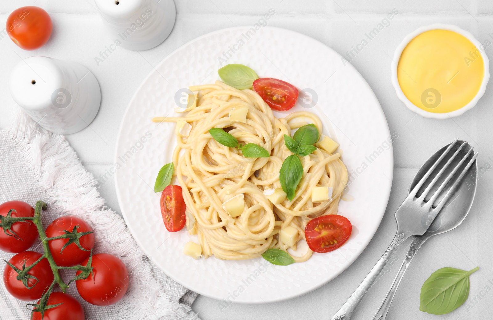 Photo of Delicious pasta with brie cheese, tomatoes and basil leaves on white tiled table, flat lay