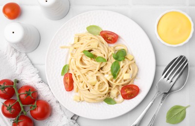 Photo of Delicious pasta with brie cheese, tomatoes and basil leaves on white tiled table, flat lay