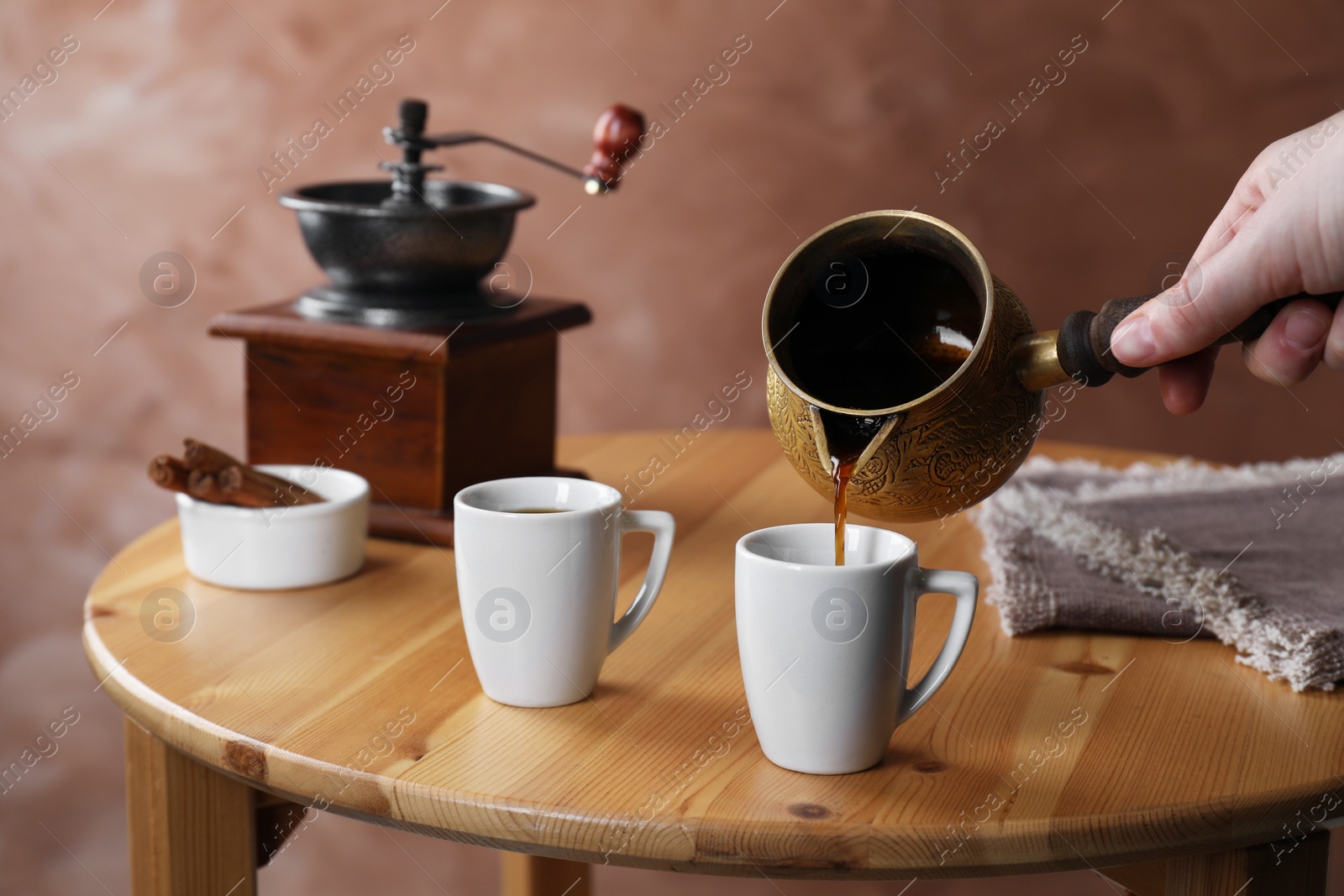 Photo of Turkish coffee. Woman pouring brewed beverage from cezve into cup at wooden table, closeup