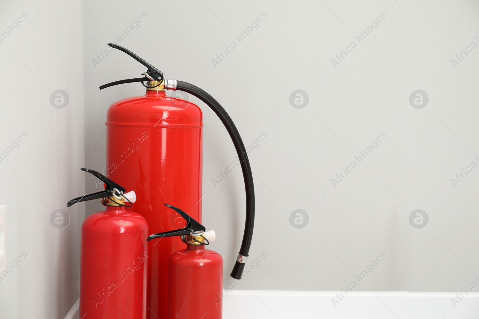 Photo of Fire extinguishers near light grey wall, space for text