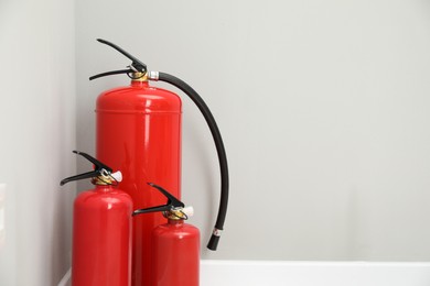 Photo of Fire extinguishers near light grey wall, space for text