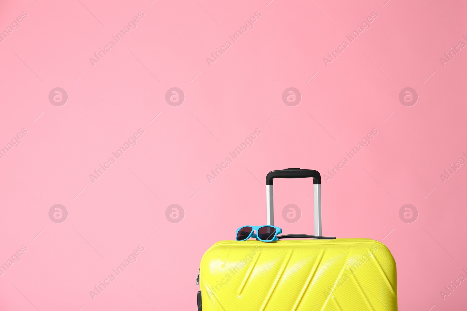 Photo of Modern yellow suitcase and sunglasses on light pink background. Space for text