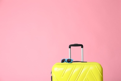 Modern yellow suitcase and sunglasses on light pink background. Space for text