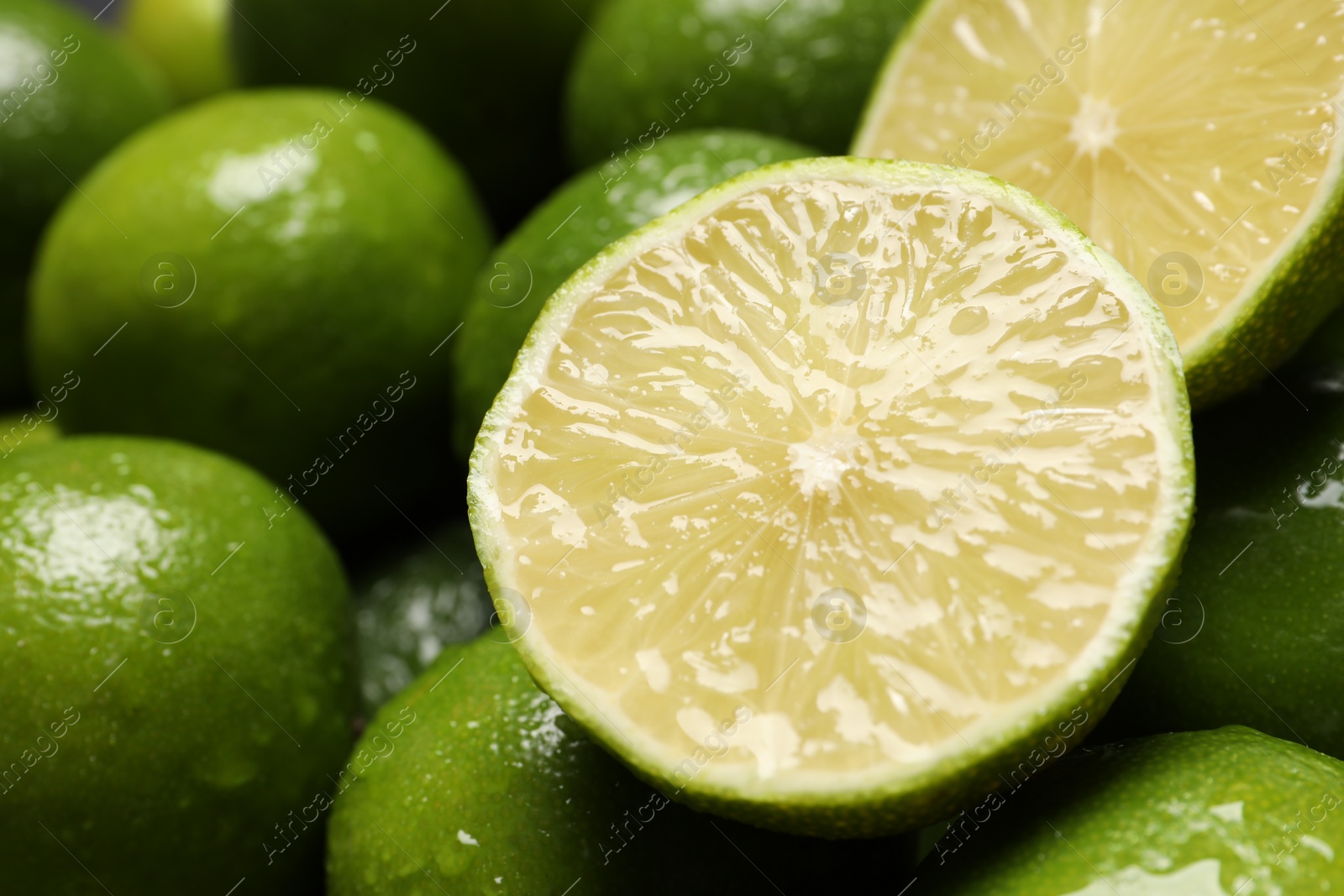 Photo of Whole and cut fresh limes with water drops as background, closeup