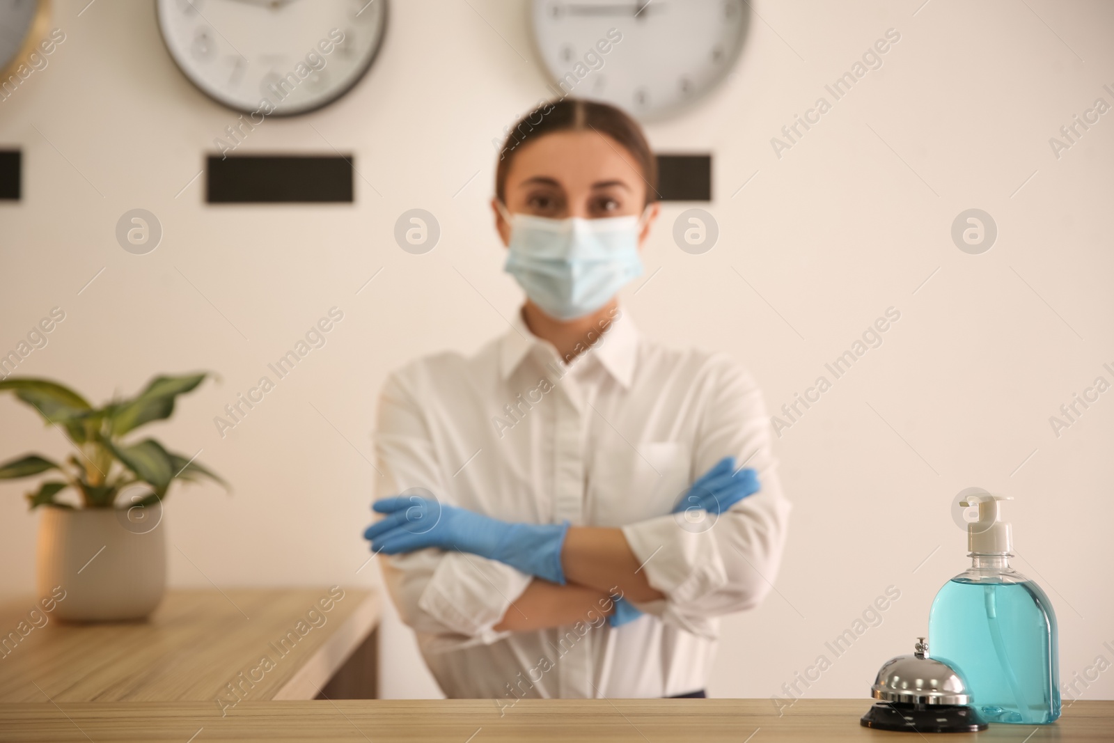 Photo of Receptionist at countertop in hotel, focus on dispenser bottle with antiseptic gel and service bell