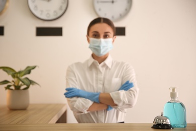 Receptionist at countertop in hotel, focus on dispenser bottle with antiseptic gel and service bell