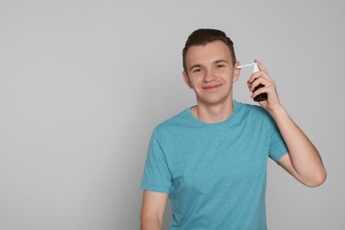 Young man using ear spray on light grey background. Space for text