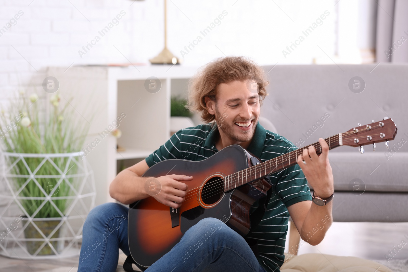 Photo of Young man playing acoustic guitar in living room
