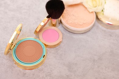 Photo of Bronzer, powder, blusher, brush and rose flower on grey textured table, above view