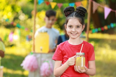 Photo of Cute little girl with natural lemonade in park, space for text. Summer refreshing drink