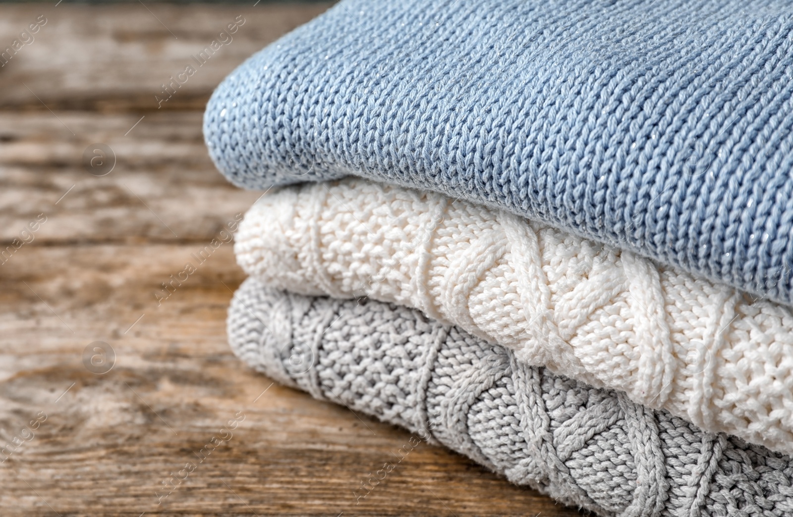 Photo of Stack of folded knitted sweaters on table, closeup