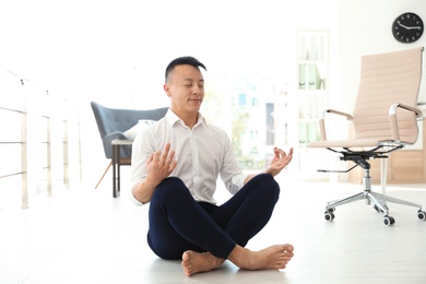 Photo of Young businessman doing yoga in office. Workplace fitness