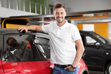 Handsome man near new car in modern auto dealership
