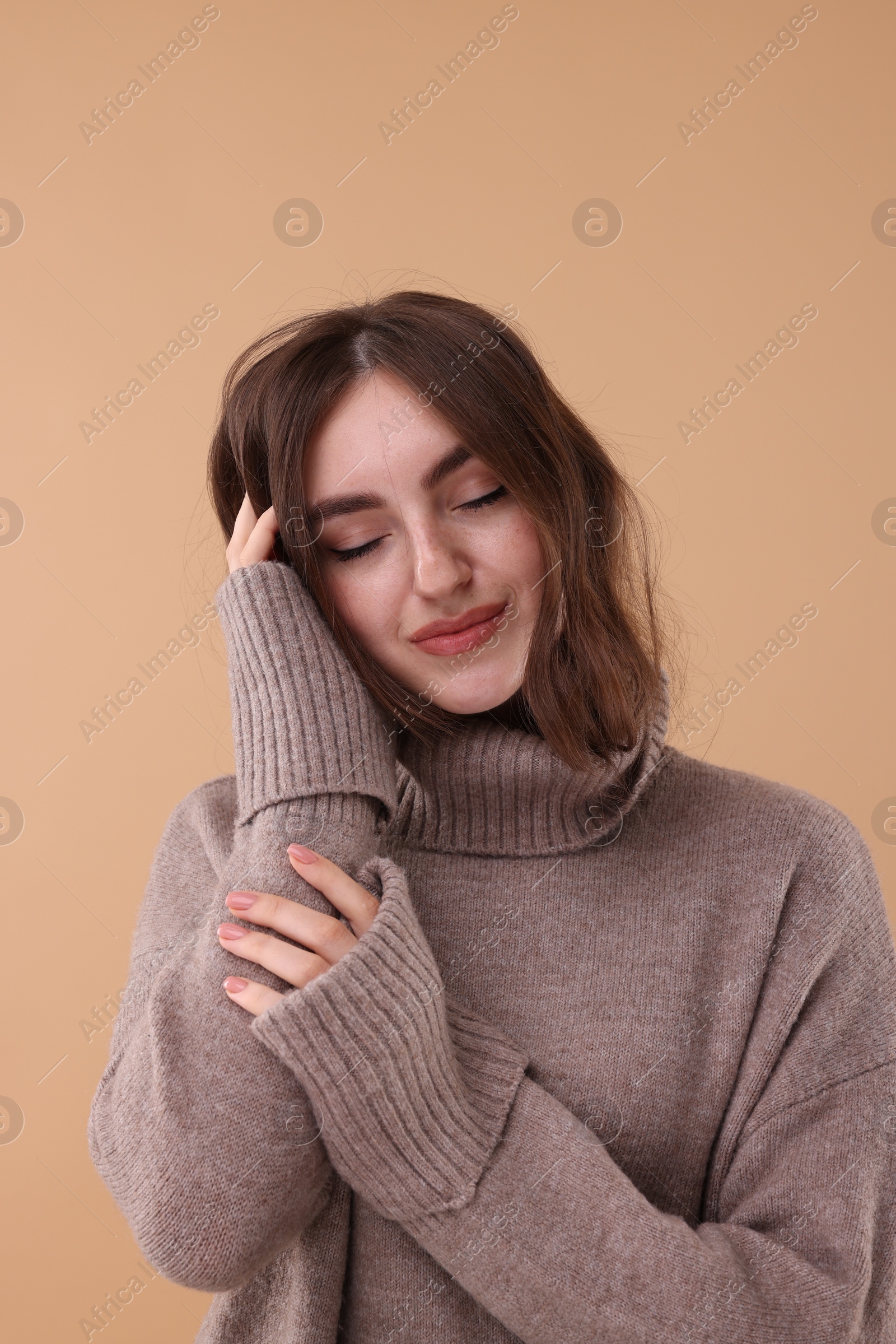 Photo of Portrait of beautiful young woman in warm sweater on brown background