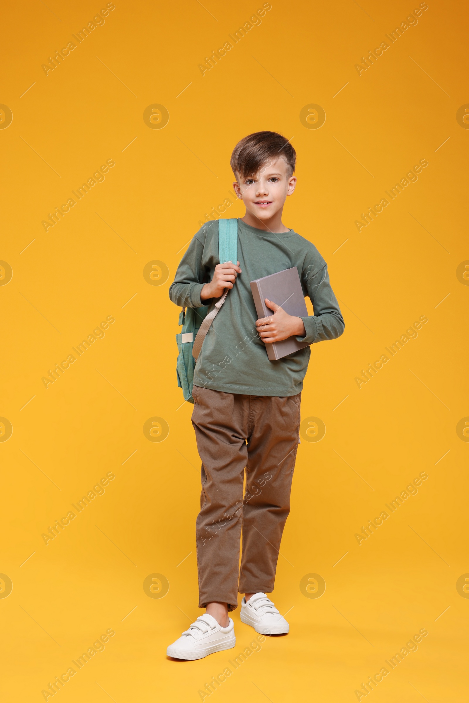 Photo of Cute schoolboy with book on orange background