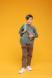 Photo of Cute schoolboy with book on orange background