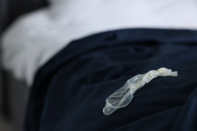 Photo of Unrolled condom on bed in bedroom, space for text. Safe sex
