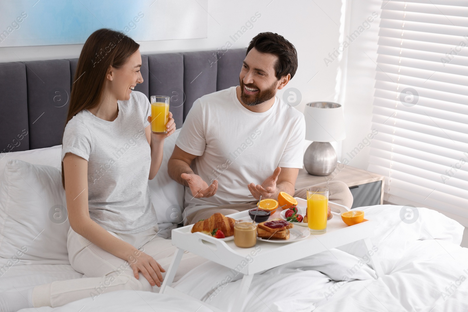 Photo of Happy couple having breakfast and talking on bed at home