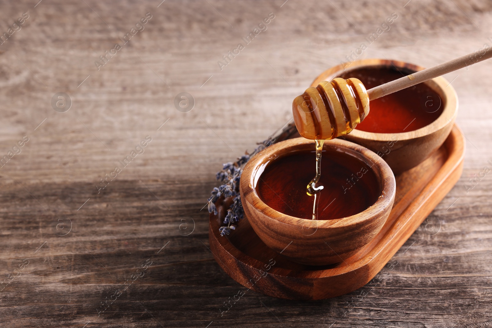 Photo of Pouring delicious honey from dipper into bowl on wooden table. Space for text