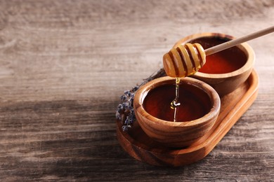 Photo of Pouring delicious honey from dipper into bowl on wooden table. Space for text