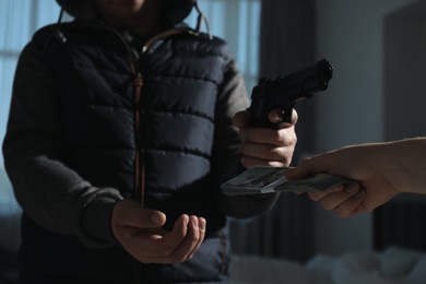 Photo of Woman giving money to criminal with gun indoors, closeup. Armed robbery