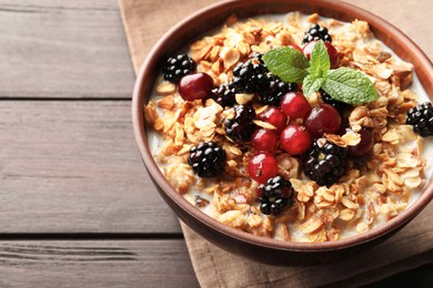 Photo of Bowl of muesli served with berries and milk on wooden table, closeup. Space for text