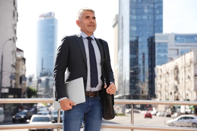 Photo of Portrait of handsome businessman with laptop in city, space for text