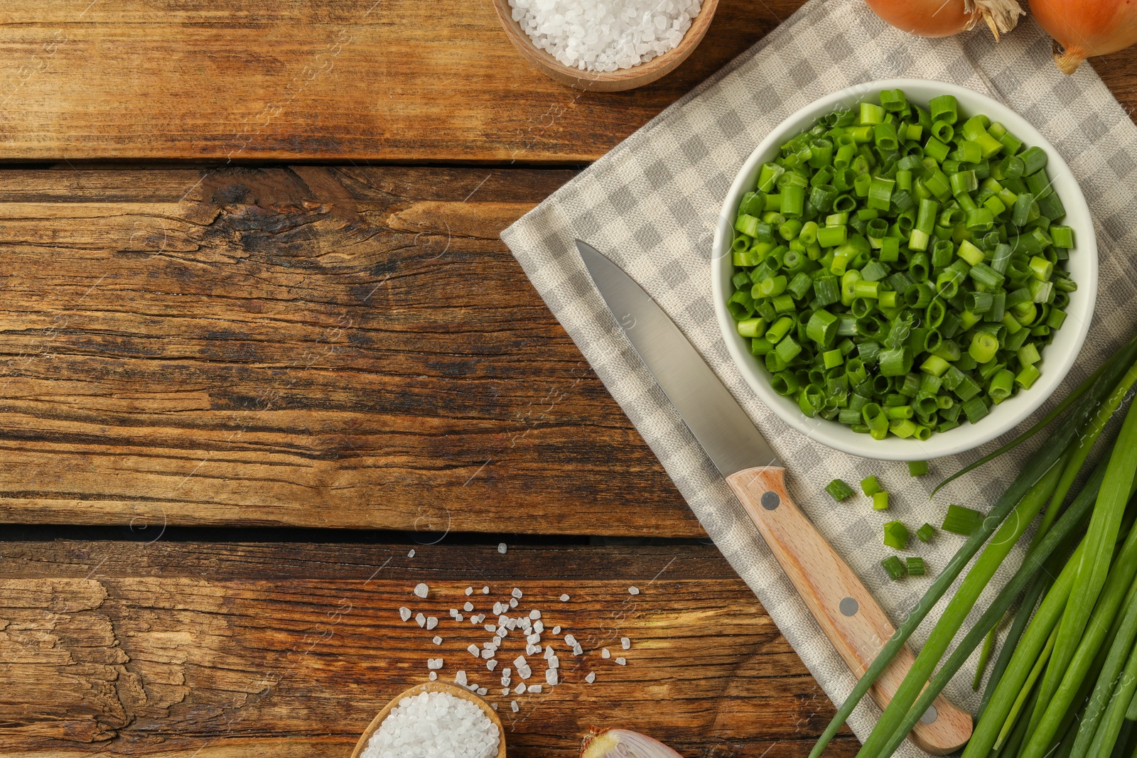 Photo of Chopped green onion in bowl on wooden table, flat lay. Space for text