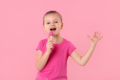 Cute little girl with lollipop on pink background