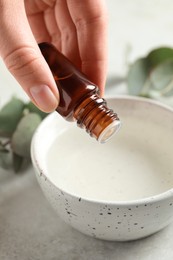 Photo of Woman dripping eucalyptus essential oil from bottle into bowl at white table, closeup