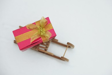 Wooden sleigh with gift box on snow outdoors, above view. Space for text