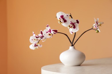 Photo of Vase with orchid flowers on white table near light brown wall. Space for text