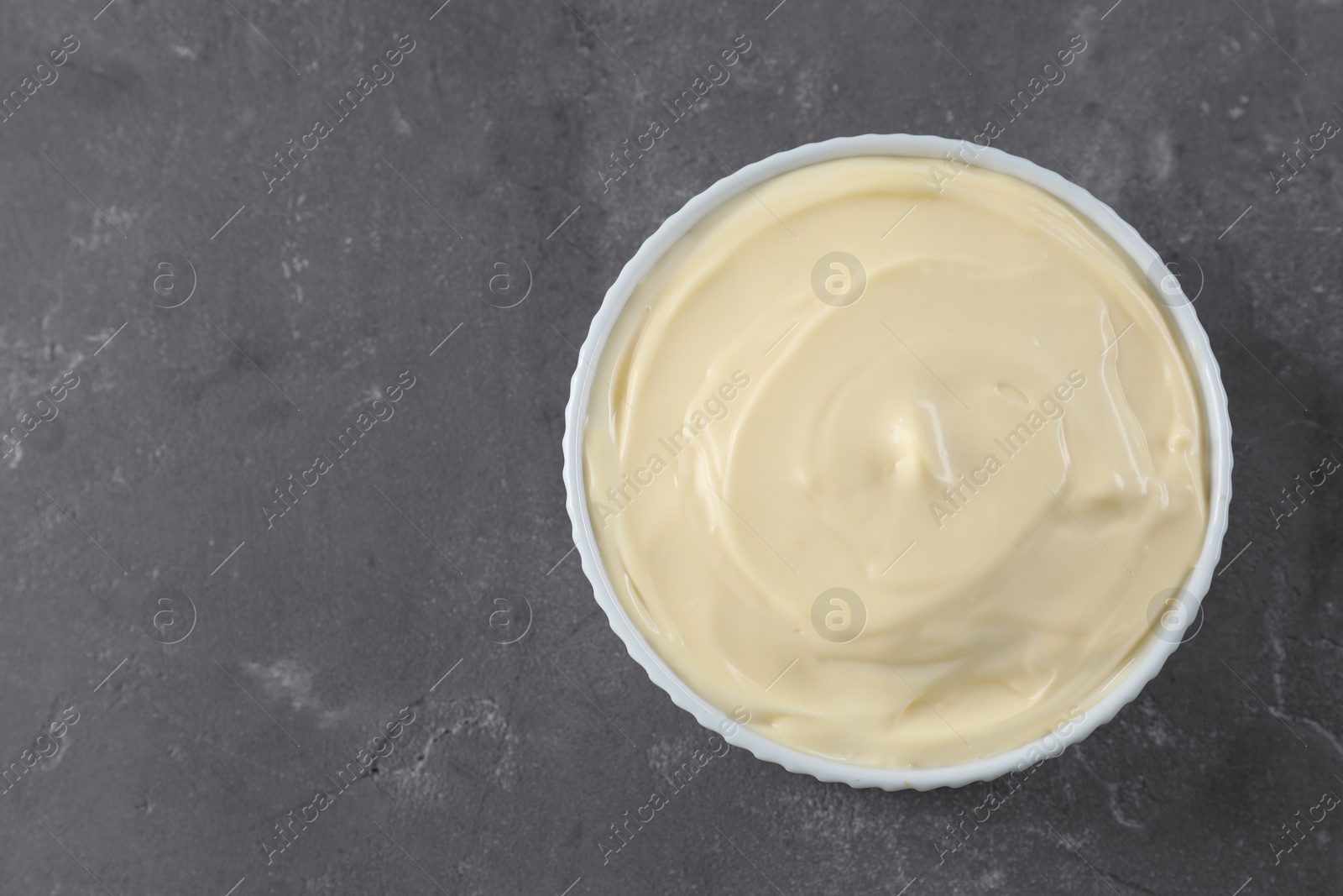 Photo of Fresh mayonnaise sauce in bowl on grey table, top view. Space for text