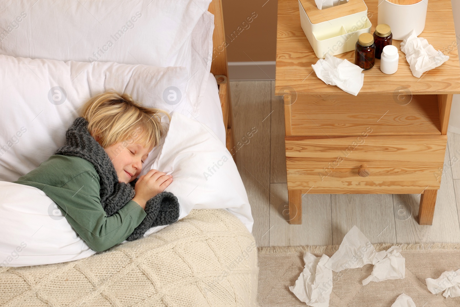 Photo of Sick boy lying in bed near bunch of napkins on floor at home, above view