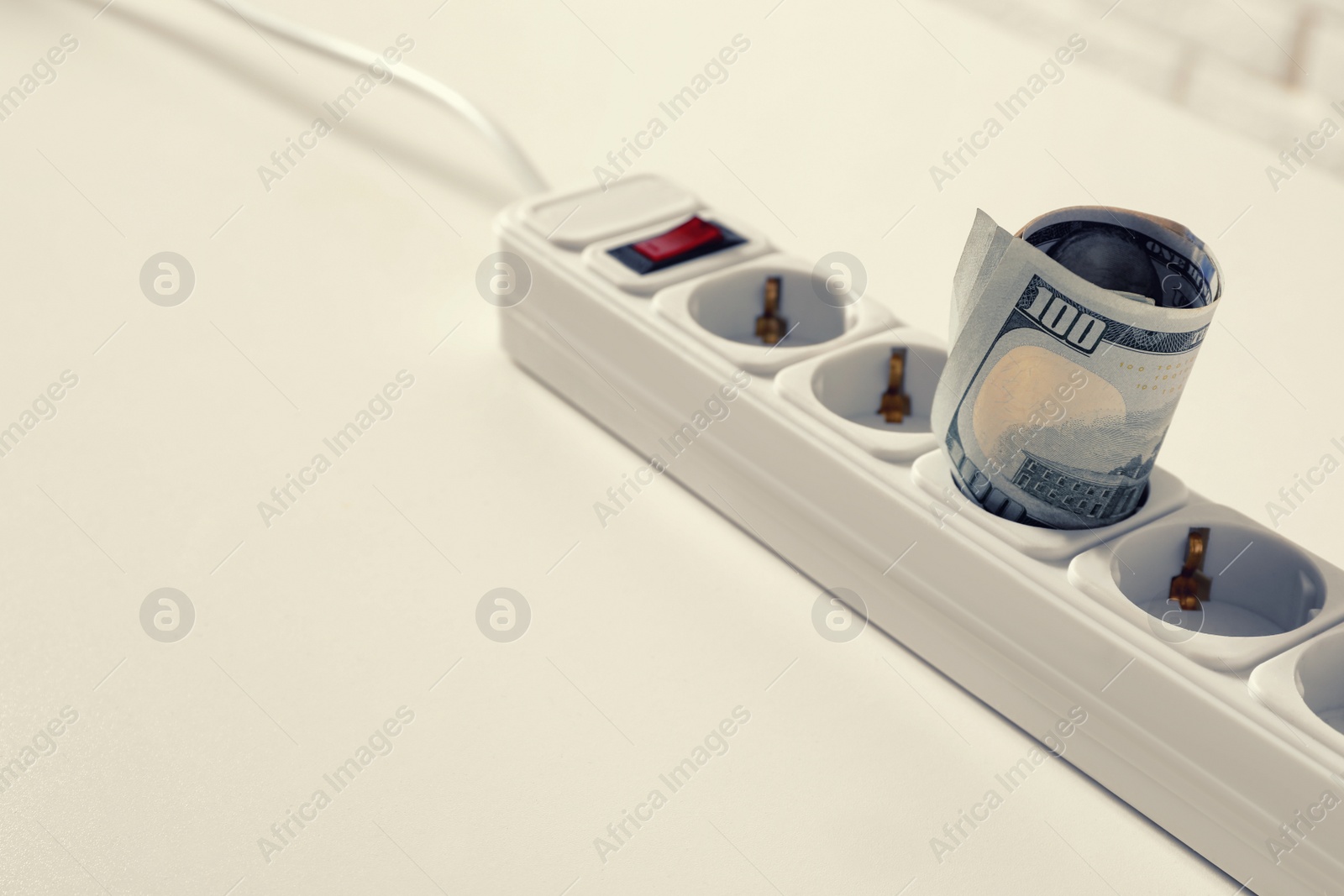 Photo of Extension board with rolled dollar banknotes on white table, closeup