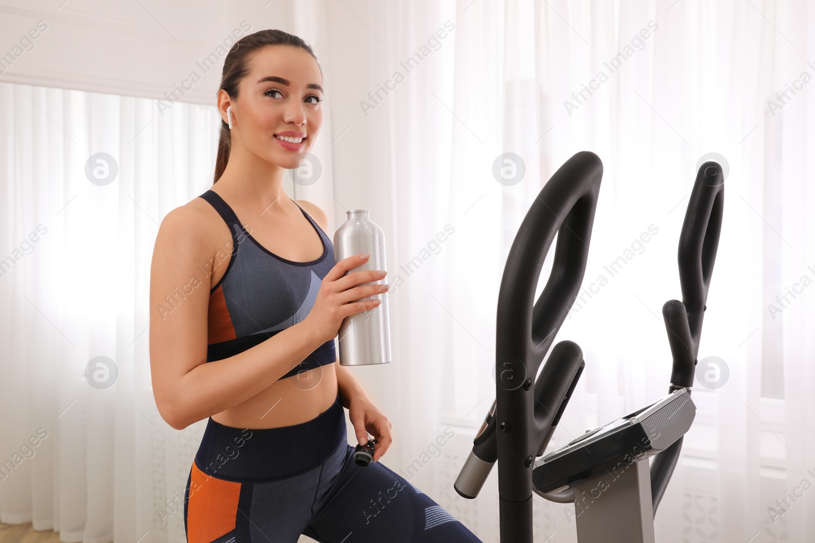 Photo of Woman with bottle on modern elliptical machine at home