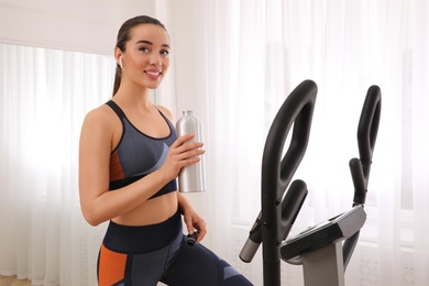 Woman with bottle on modern elliptical machine at home
