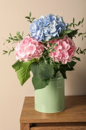 Photo of Beautiful hortensia flowers in can on wooden table against beige background