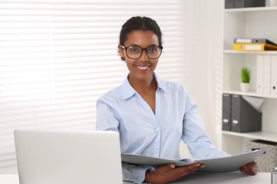 African American intern with folder working at white table in office