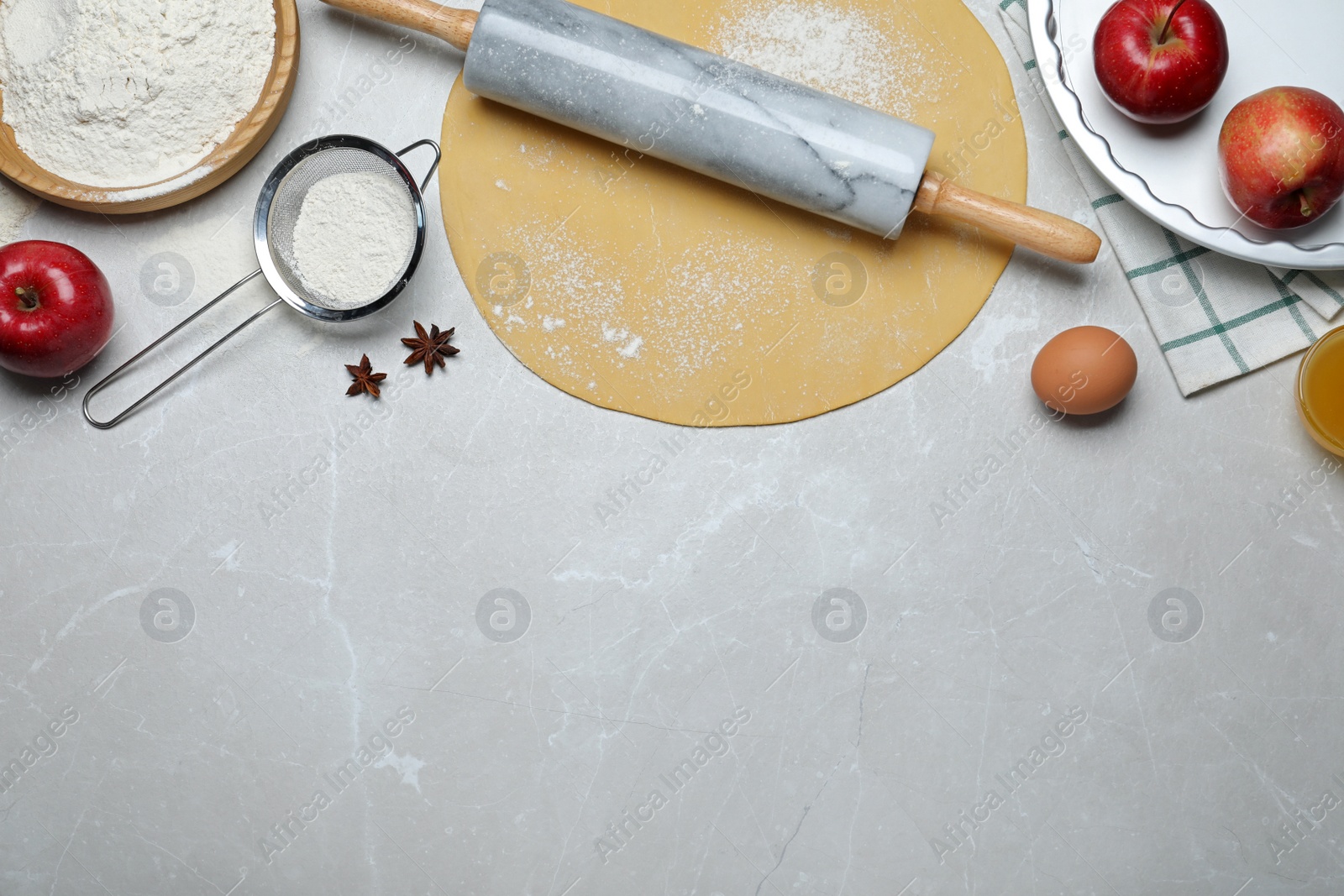 Photo of Flat lay composition with raw dough and ingredients on light grey table, space for text. Baking apple pie