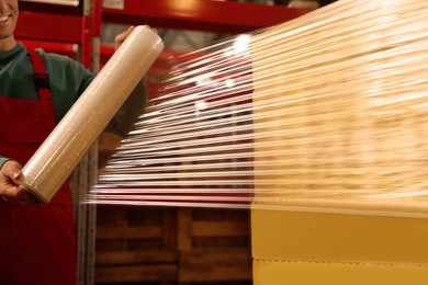 Worker wrapping boxes in stretch film at warehouse, closeup