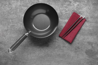 Empty iron wok and chopsticks on grey table, flat lay