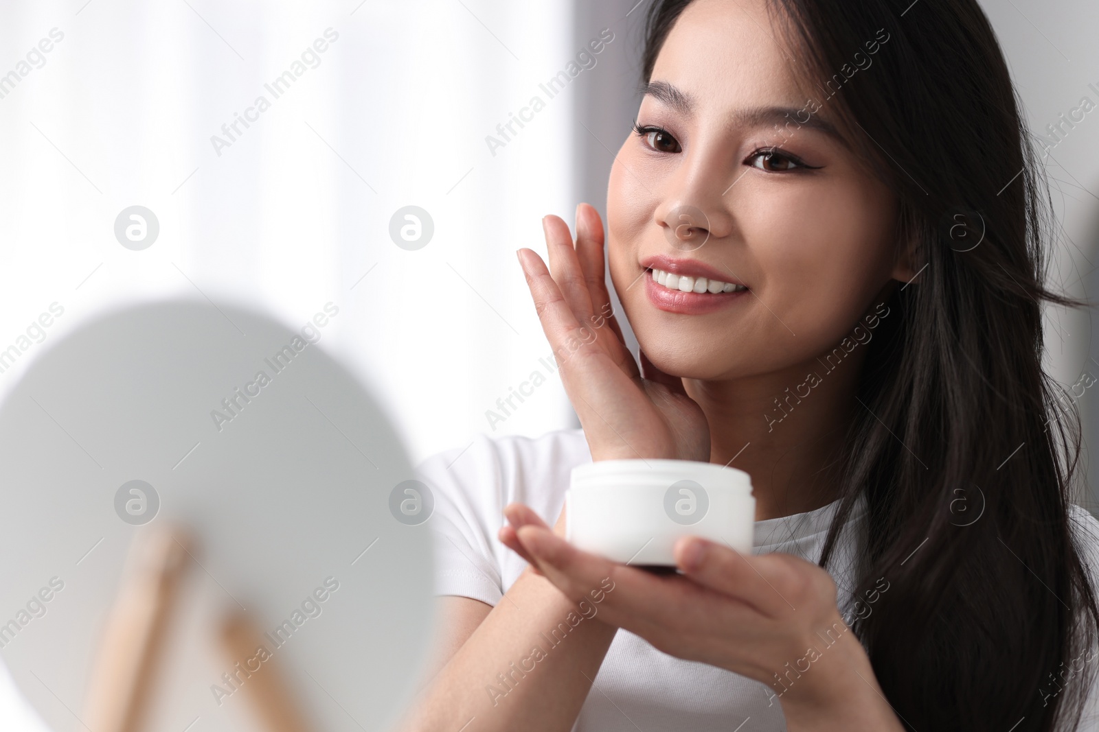 Photo of Happy woman applying face cream at home, space for text